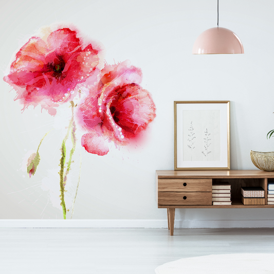 A minimalist living room with a large Decor2Go Wallpaper Mural of Red Poppies Watercolor on a white wall, a wooden sideboard with books, a framed picture, and a plant beneath a hanging pink lamp.