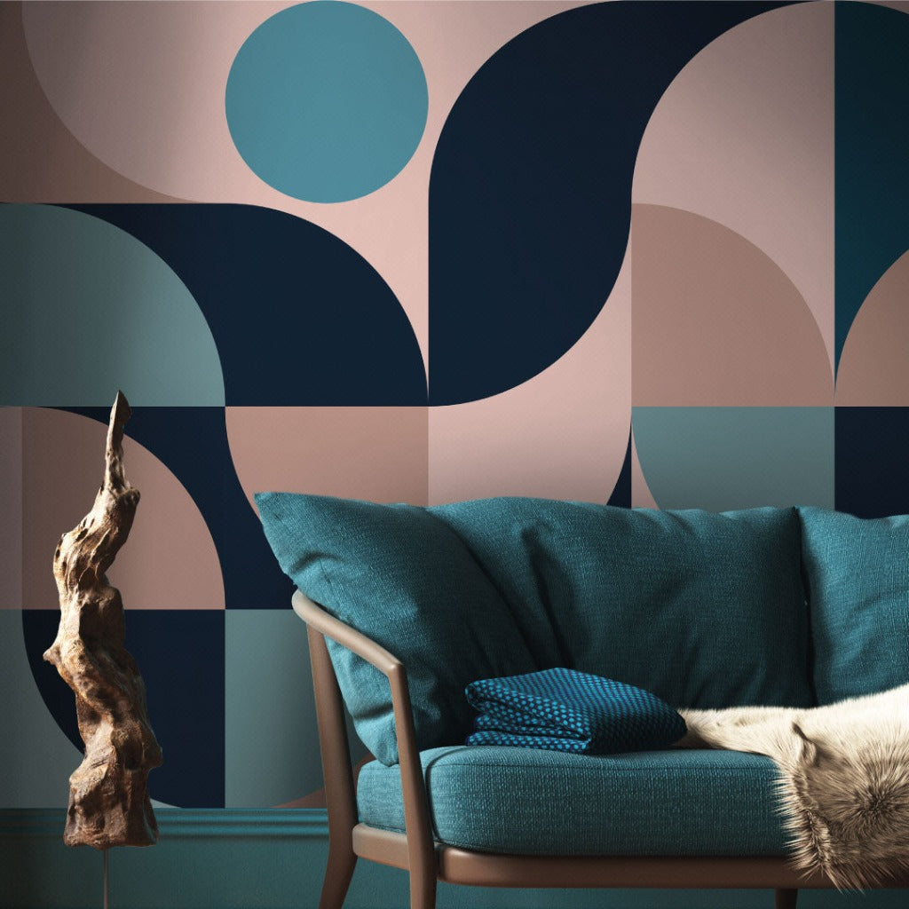 A stylish living room corner featuring a Retro Style 60s Mural Wallpaper in soft colors of teal, pink, and beige, with a teal sofa adorned by textured pillows, and a unique wooden sculpture beside it by Decor2Go Wallpaper Mural.