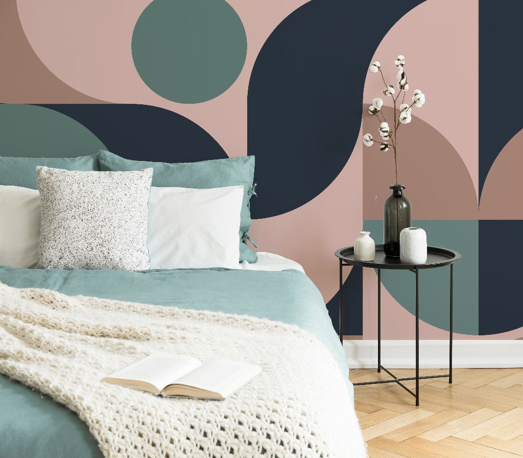 A cozy bedroom featuring a bed with a teal blanket and white knit throw, a Decor2Go Wallpaper Mural Retro Style 60s Mural, and a black side table with decorative vases and flowers.