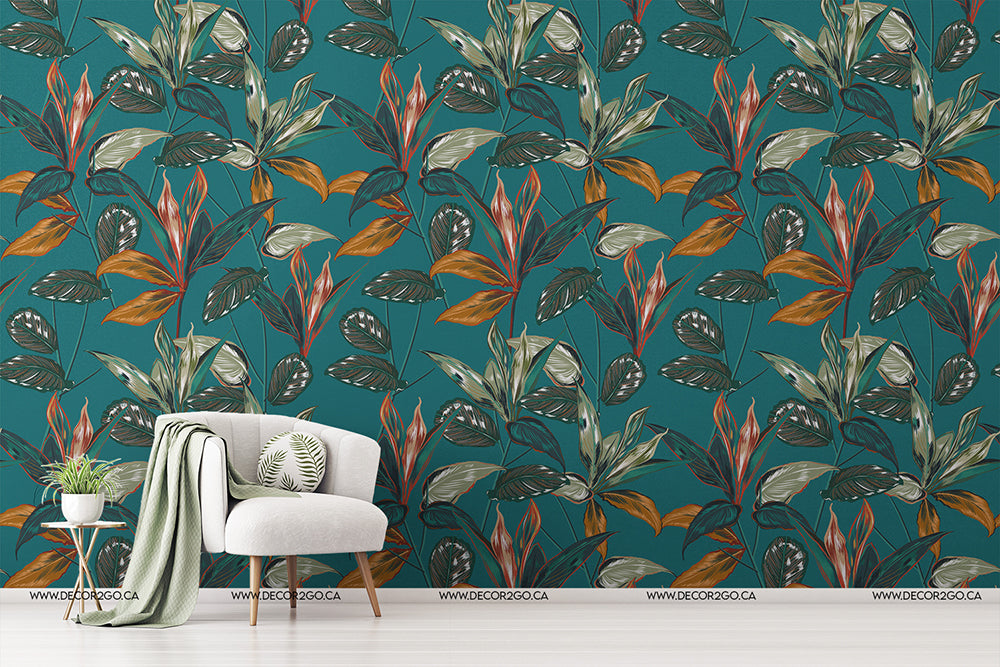 A modern living room with a vibrant Decor2Go Wallpaper Mural featuring large tropical leaves in shades of green, orange, and brown. A cozy white chair with a green cushion and a matching throw sits beside a small