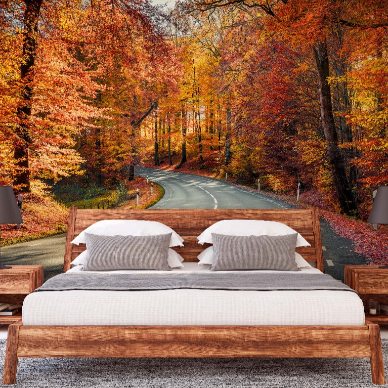 A modern bedroom with a large bed and wooden nightstands. The wall behind the bed features an eye-catching Decor2Go Wallpaper Mural of a curving road surrounded by autumn-colored trees.
