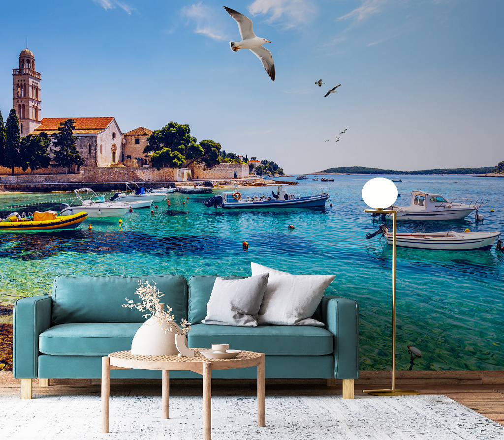 A scenic Decor2Go Wallpaper Mural depicting a serene Italian Riviera coastal scene with boats and a church, overlaid with a modern living room setup featuring a green sofa and a small wooden table.