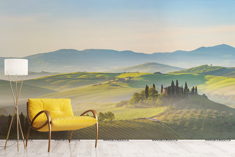 A stylish modern yellow armchair and a white floor lamp in front of a large window depicting a vibrant Tuscany mural with Decor2Go Wallpaper Mural of Rolling Hills at sunrise.