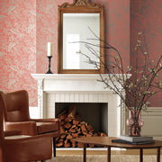 Living Room - A cozy features a white fireplace with firewood, a large ornate mirror above it, York Wallcoverings' Rose Canopy Wallpaper in pink floral, a leather armchair, and a wooden coffee table with a vase of bare branches