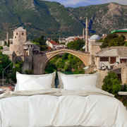 Bedroom - A creative bedroom setup where the bed appears to overlook a scenic historical city with an ancient stone bridge, mosque, and lush mountains in the background, all captured beautifully on a Decor2Go Wallpaper Mural.