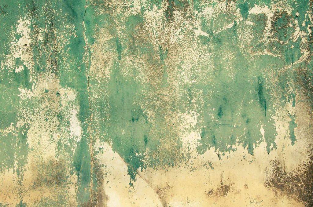 A weathered, textured wall painted in shades of green and beige. The paint is chipped and peeling, revealing layers of color and worn surfaces underneath, reminiscent of a Rusti rust Weathered Concrete mural wallpaper often found in art or design studios by Decor2Go Wallpaper Mural.