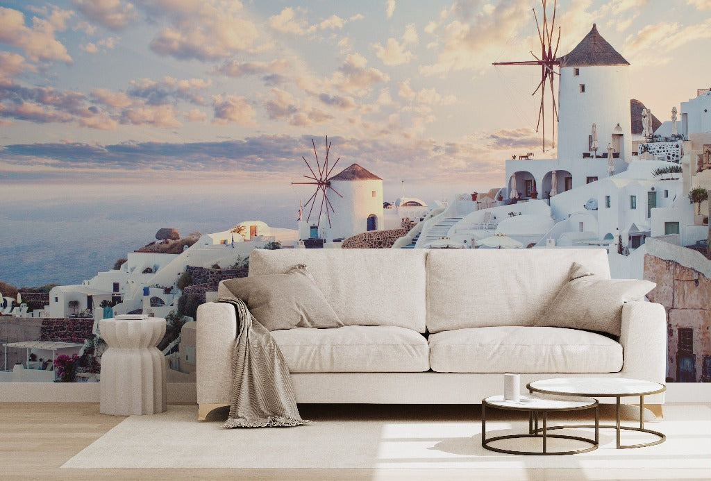 Living Room - A modern living room with a white sofa and small tables in front of a large window displaying a Decor2Go Wallpaper Mural, showing its famous white houses and windmills against a sunset sky.