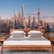 Bedroom - A modern bedroom featuring a wooden bed with white bedding and two bedside tables, set against a large Decor2Go Wallpaper Mural of the Shanghai Skyline at sunset.