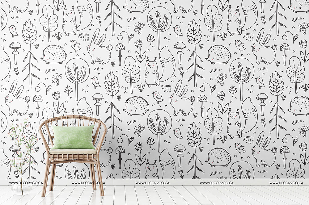 A minimalist room featuring a wooden chair with a green cushion against a white Decor2Go Wallpaper Mural with a black doodle pattern of various whimsical flora and fauna.