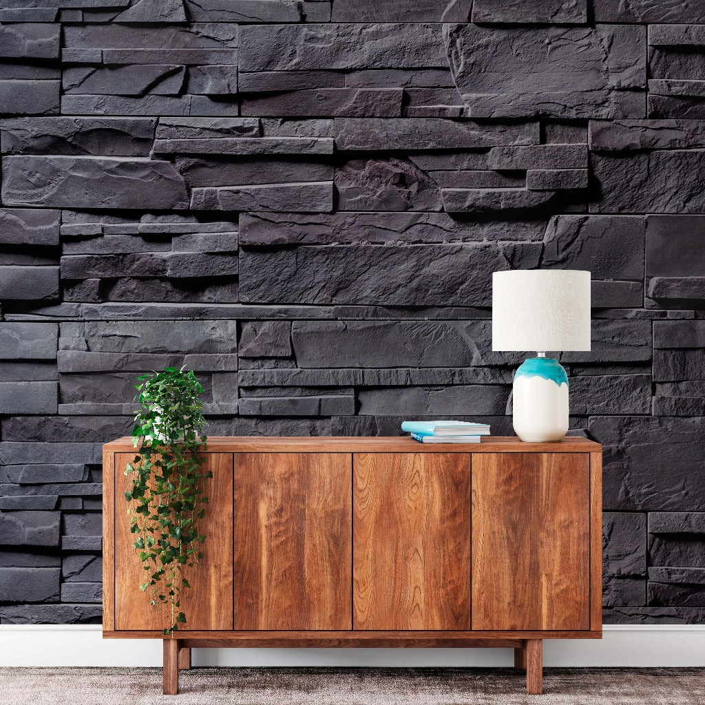 A stylish wooden sideboard against a Decor2Go Wallpaper Mural, with a white lamp, blue vase, books on top, and a hanging green plant on the left.