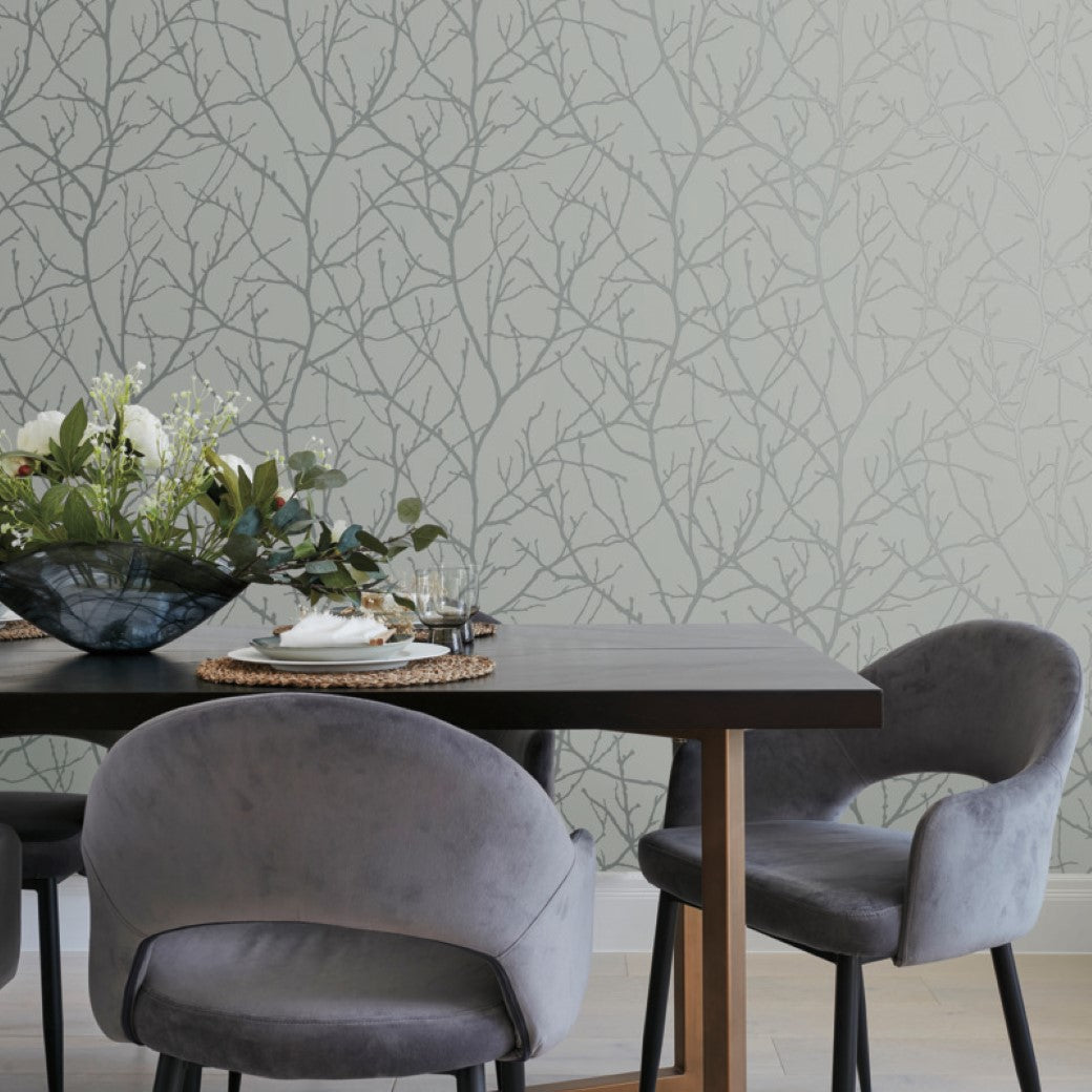 Dining Room - A area showcases a modern touch with a dark wooden table and two gray chairs. The table is set with a floral arrangement, glasses, and plates, while the backdrop features York Wallcoverings' Smokey Blue & Silver Trees Silhouette Wallpaper