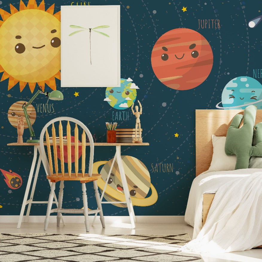A children's bedroom corner with a Decor2Go Wallpaper Mural Solar System theme, featuring educational wallpaper with cartoon planets and stars, a wooden chair, a small table with books, and a bed with a green pillow.