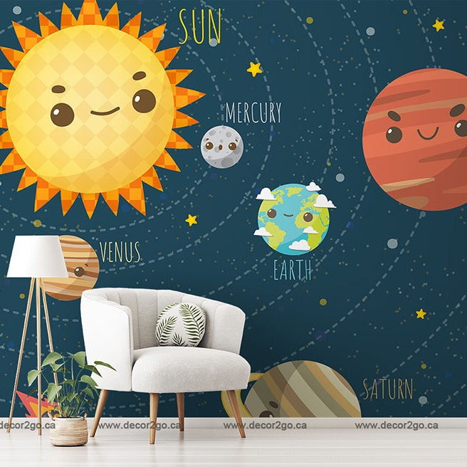 A playful Decor2Go Wallpaper Mural depicting cartoon-style planets with facial expressions and names, including a smiling sun. A white chair, lamp, and potted plant are in front of the wallpaper.