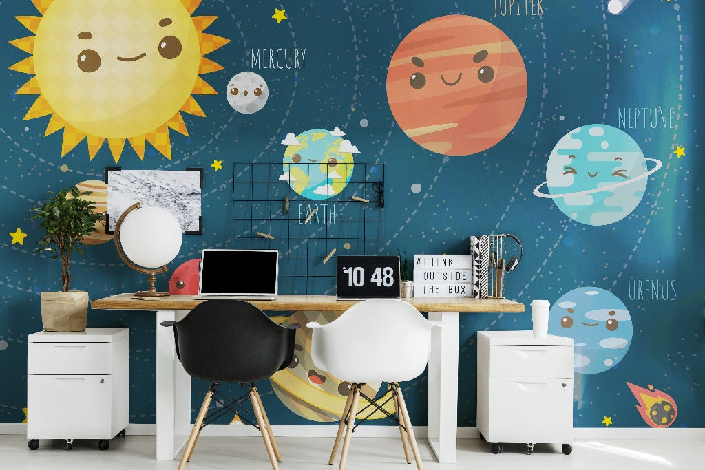 A vibrant children's study room with Decor2Go Wallpaper Mural featuring colorful planets and stars. A wooden desk with a computer, clock, and decor items, flanked by two chairs.