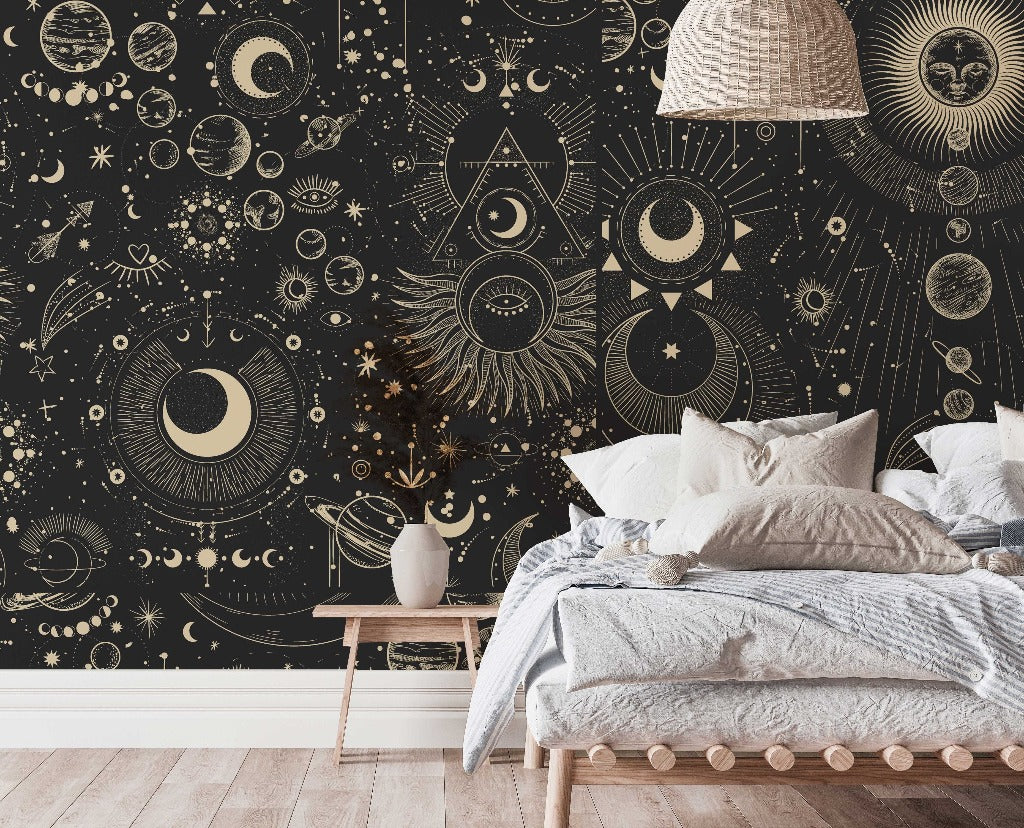 A stylish bedroom featuring a large bed with white bedding and a wall adorned with an intricate Decor2Go Wallpaper Mural, showcasing suns, moons, and stars in gold on a black background.