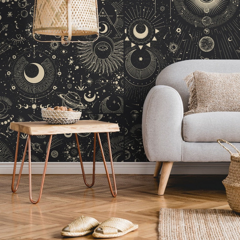 A cozy living room corner with a gray armchair and a wooden side table on copper legs, against a black Decor2Go Wallpaper Mural. A woven rug, slippers, and a wicker basket complete.