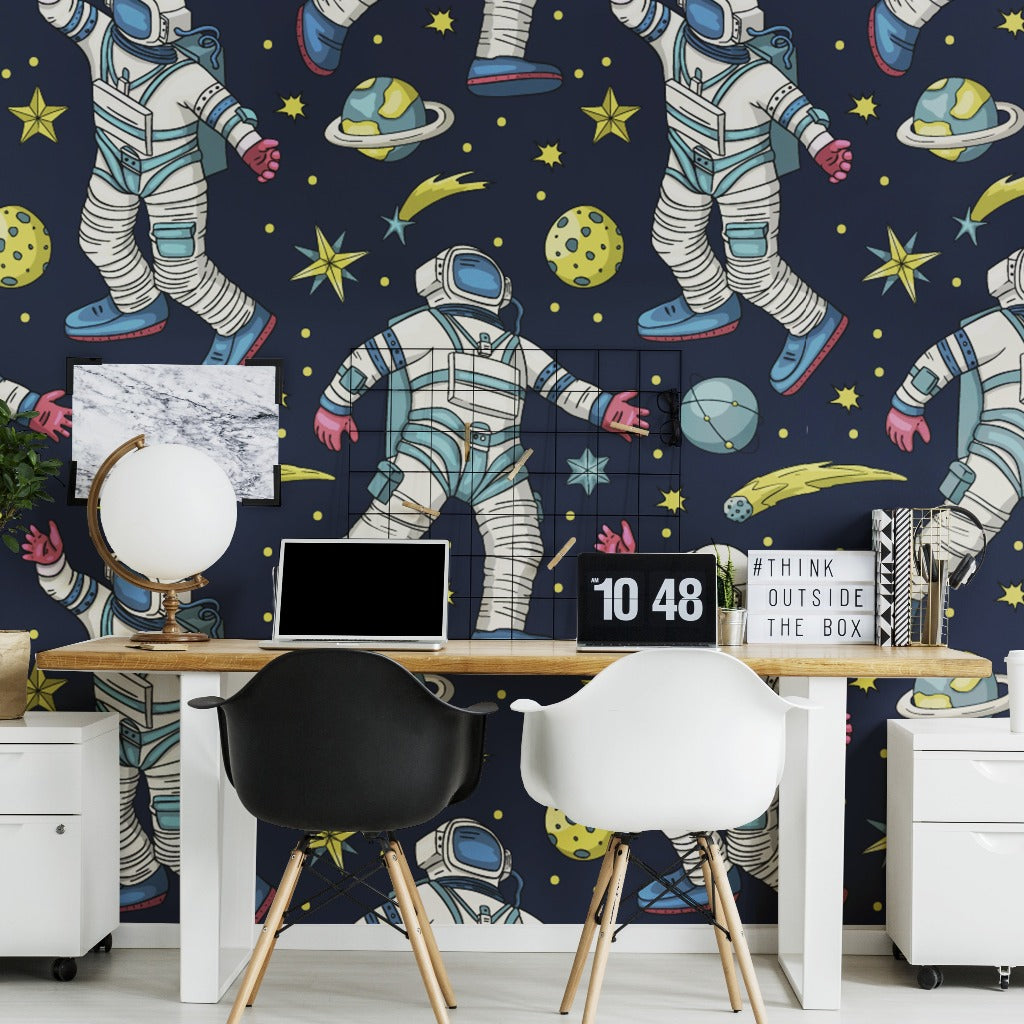 Home Office - A vibrant home office with a wall covered in Decor2Go Wallpaper Mural featuring astronauts and planets. The desk holds a laptop, a small globe, and a decorative sign, flanked by two modern chairs.
