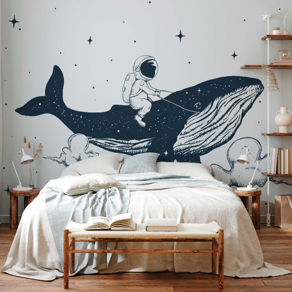 A whimsical children's bedroom with a large Decor2Go Wallpaper Mural featuring an astronaut riding a whale in space, embodying a dream-like aesthetic. The room includes a neatly made bed, wooden bench, and floating