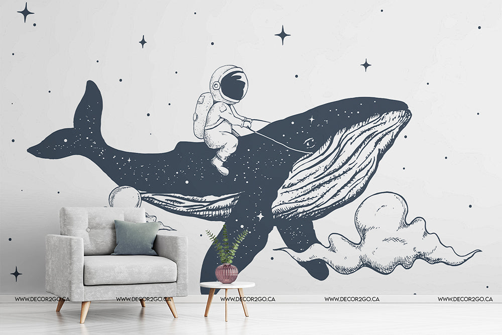 Illustrative Space Whale Wallpaper Mural depicting an astronaut riding a space whale through a star-filled sky, set in a modern living room with a grey armchair and small plant by Decor2Go Wallpaper Mural.