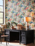 A cozy study area featuring a black wooden desk, a patterned armchair, and removable Summerhouse Midnight Wallpaper Orange, Green (60 Sq.Ft.) by York Wallcoverings with vibrant red and green foliage. A vintage-style lamp and decor items adorn the desk.