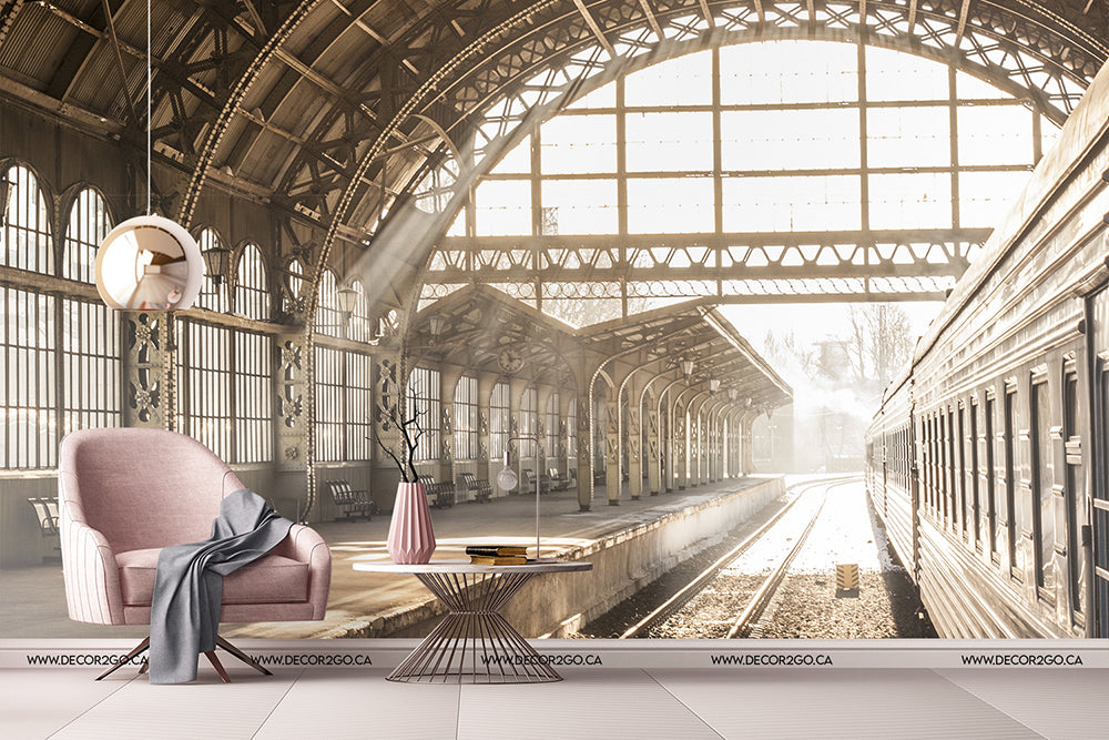 A conceptual design of a vintage railway station transformed into a stylish living space features a modern pink chair, sleek floor lamp, and elegant Decor2Go Wallpaper Mural under a grand arched roof with sunlit tracks.