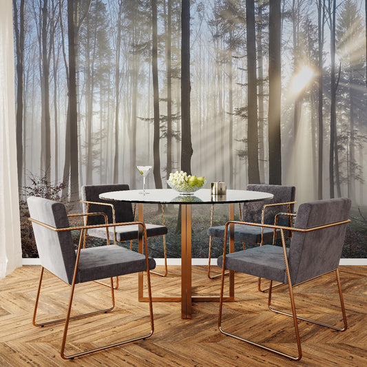 A modern dining area showcases a round glass table with four gray chairs, enhanced by Decor2Go's Sun Rays Through the Forest Wallpaper Mural. Sunlight filters through trees, illuminating a wine glass and a flower vase on herringbone wood flooring.