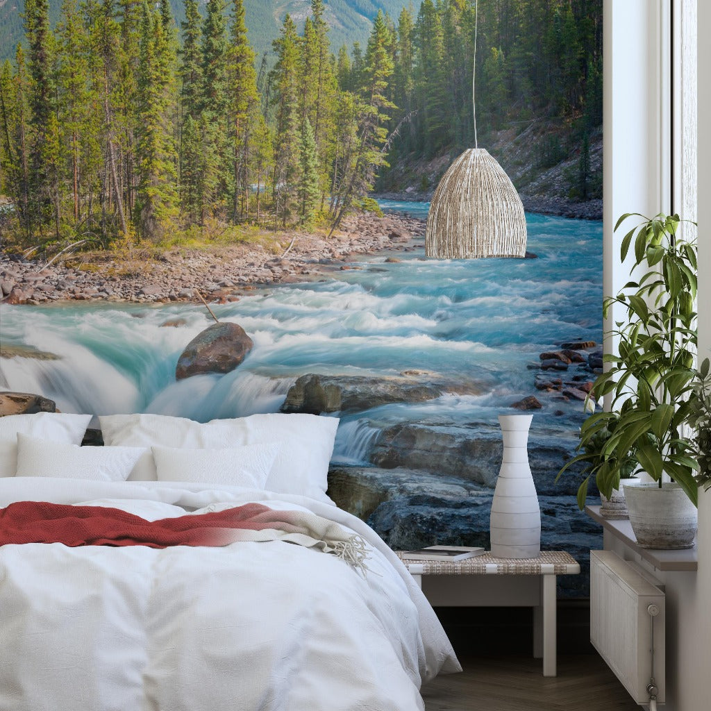 A cozy bedroom with a large Decor2Go Wallpaper Mural of Sunwapta Falls flowing through a forested mountain landscape. The room features a comfortable bed and a stylish hanging lamp.