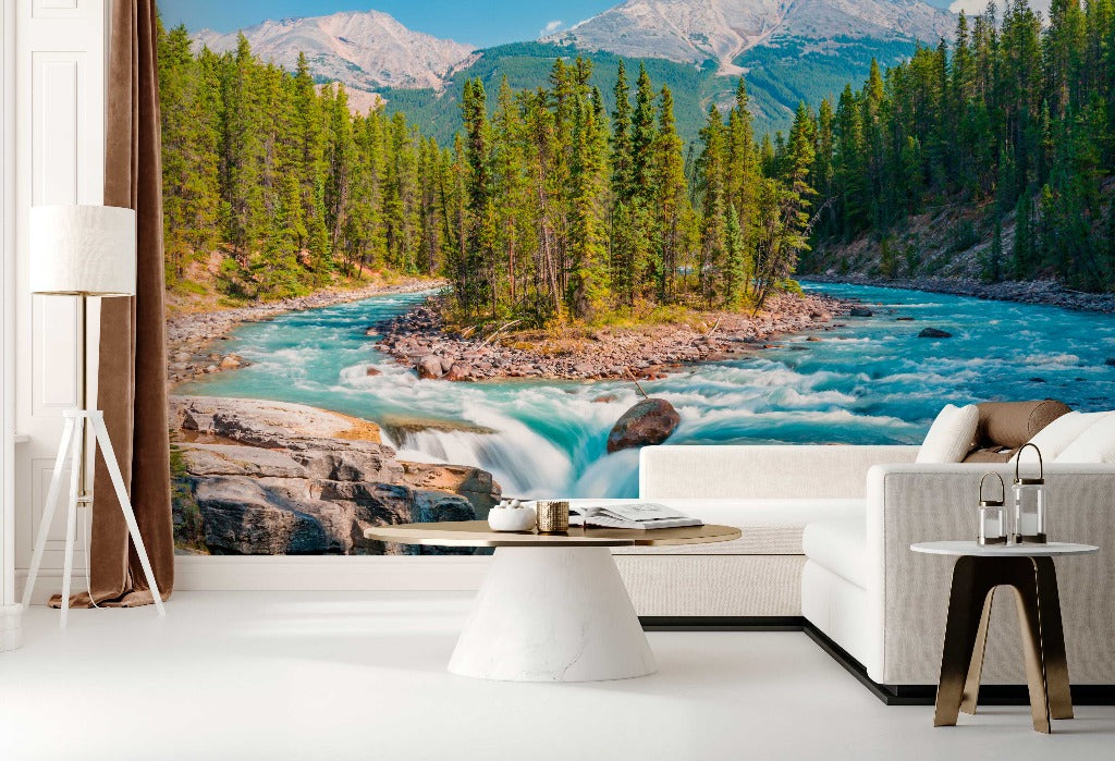 A modern living room with a large Decor2Go Wallpaper Mural depicting a vibrant river flowing through a mountainous forest landscape. The room includes a white sofa, a stylish lamp, and a small coffee