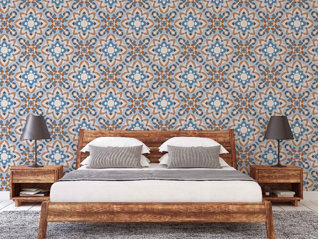 A modern bedroom featuring a wooden bed with white bedding and two pillows, flanked by wooden nightstands with gray lamps. The room has a vibrant blue and brown Decor2Go Wallpaper Mural Moroccan-style wallpaper.