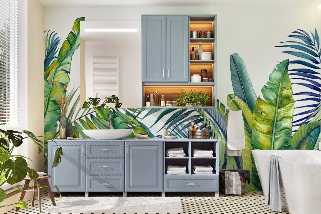 A bright, Tropical Blue Tropical Bloom Wallpaper Mural-themed bathroom with large banana leaves patterned wallpaper, blue cabinetry, and an assortment of green houseplants creating a fresh, vibrant atmosphere from Decor2Go Wallpaper Mural.