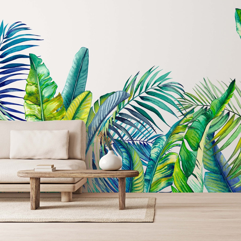 A modern living room featuring a white sofa and a wooden coffee table, against a vibrant Tropical Blue Tropical Bloom Wallpaper Mural with palm tree leaves in shades of blue and green by Decor2Go Wallpaper Mural.