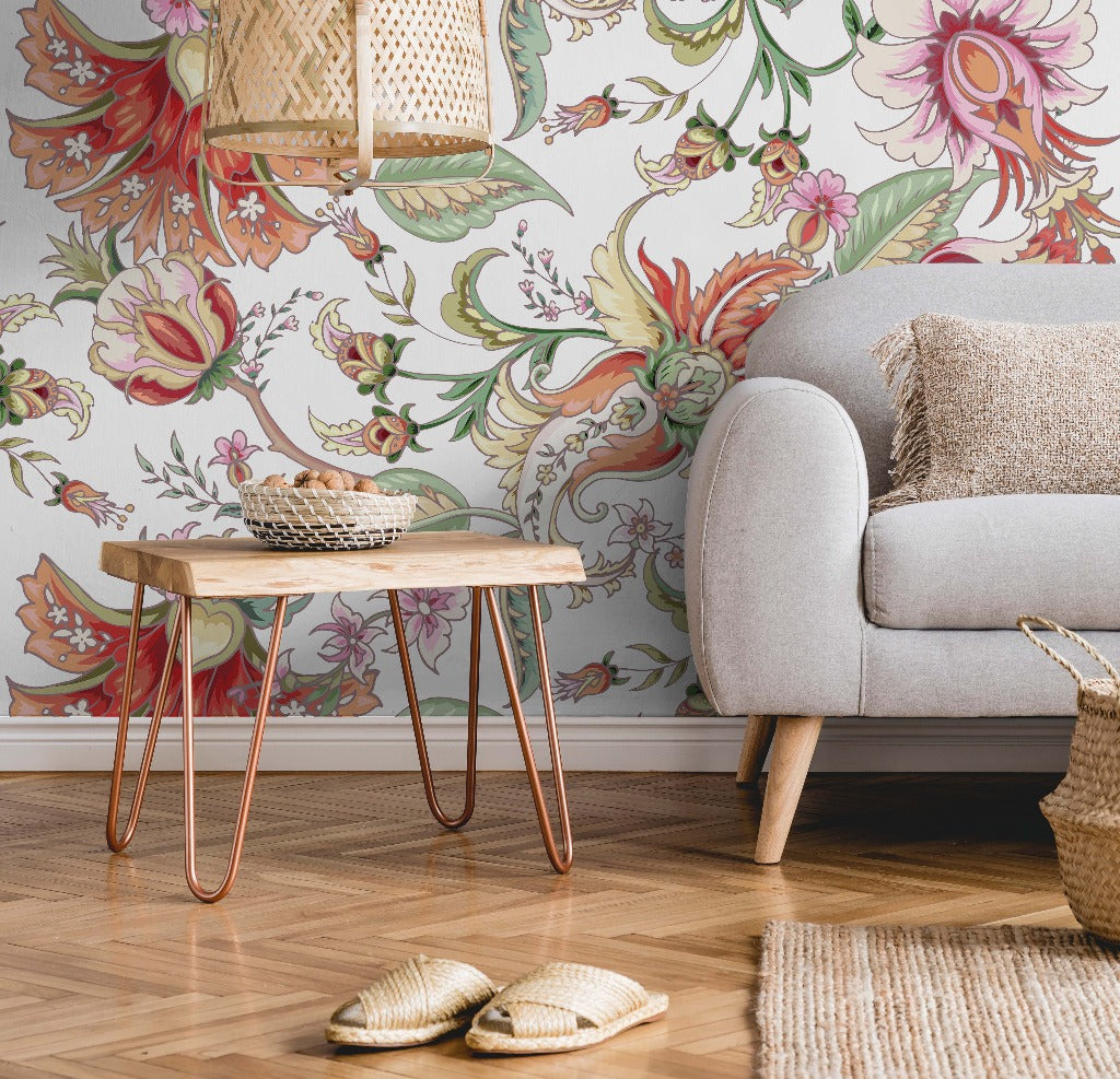 A cozy living room corner featuring a Tropical Fantasy Floral Wallpaper Mural from Decor2Go Wallpaper Mural, with a gray sofa with a beige cushion, a small wooden table with copper legs, a woven basket, and a pair of slippers on a rug.