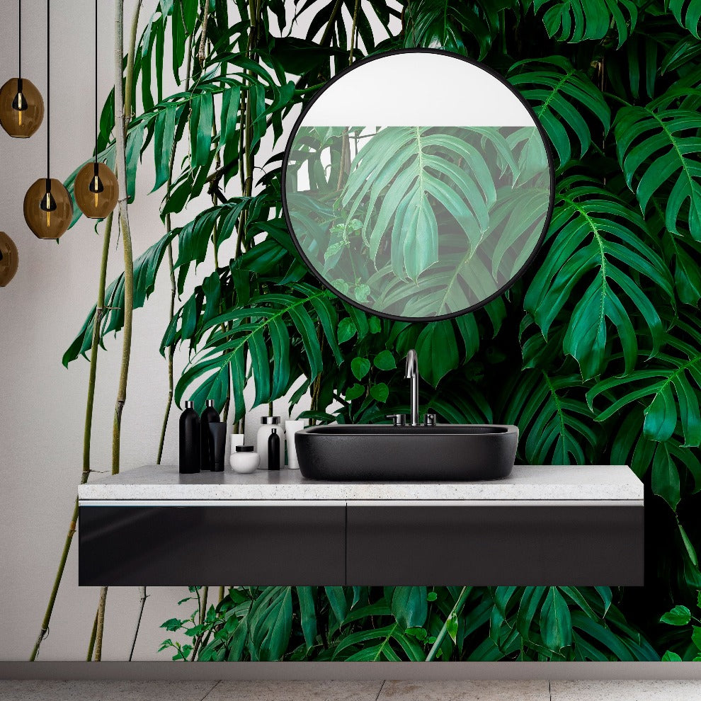 A modern bathroom vanity with a sleek black basin, surrounded by lush green plants, and a round mirror reflecting Decor2Go Wallpaper Mural's Tropical Jungle Leaves Wallpaper Mural.