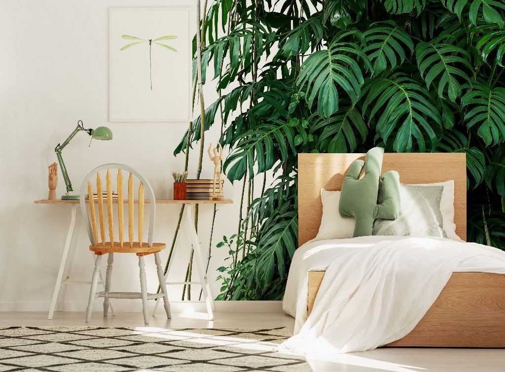 Bedroom - A bright and cozy bedroom corner with a large, leafy indoor plant, wooden bed and desk with a chair, and soothing green-themed Decor2Go Wallpaper Mural featuring the Tropical Jungle Leaves Wallpaper Mural.