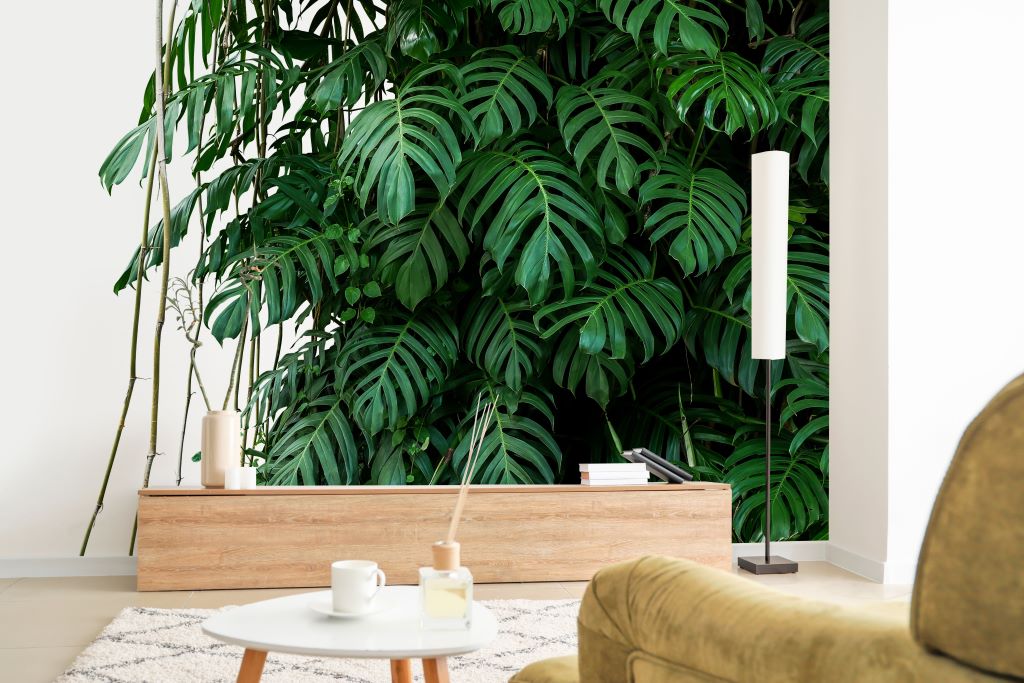 Living Room - A cozy living room corner with a Tropical Jungle Leaves Wallpaper Mural from Decor2Go Wallpaper Mural in the background, a small wooden table with candles in the foreground, and part of a comfy chair visible.