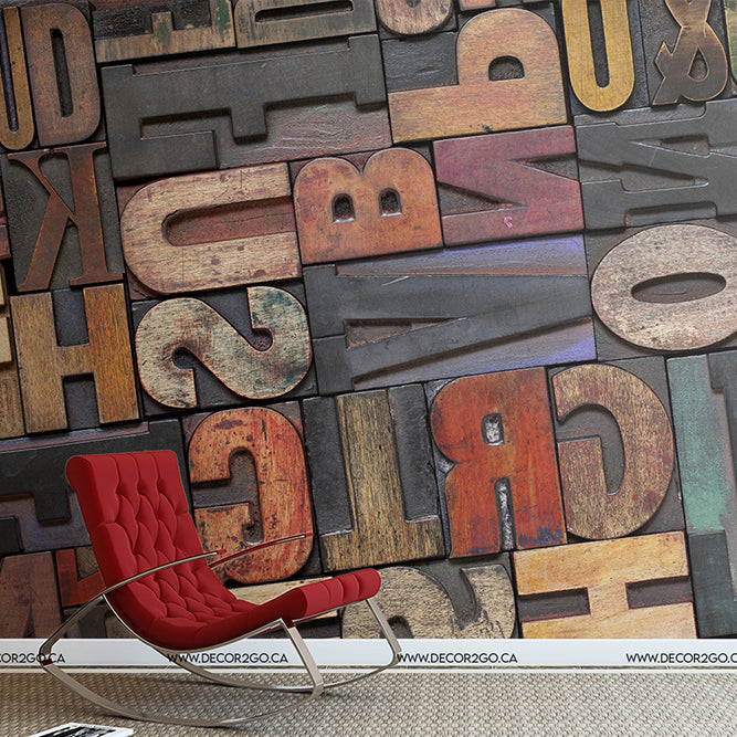 A stylish red lounge chair sits on a colorful weathered look floor composed of oversize vintage printing press letters with various fonts and colors from Decor2Go Wallpaper Mural.