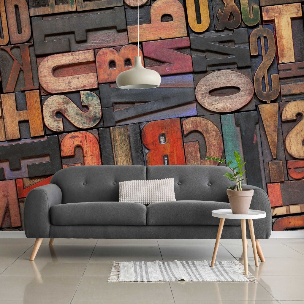 Living Room - A stylish living room with a gray sofa, decorative cushions, a small white coffee table with a potted plant, a white rug, and a large colorful Decor2Go Wallpaper Mural with various letters.