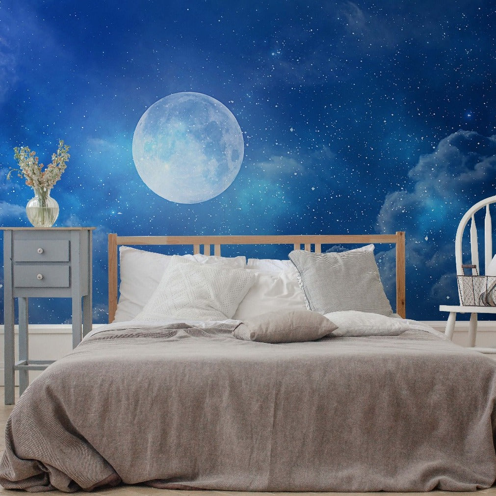 A cozy bedroom setup with a wooden bed covered in gray bedding, white and blue pillows, a white chair, and Decor2Go Wallpaper Mural under a large moonlight wallpaper mural.