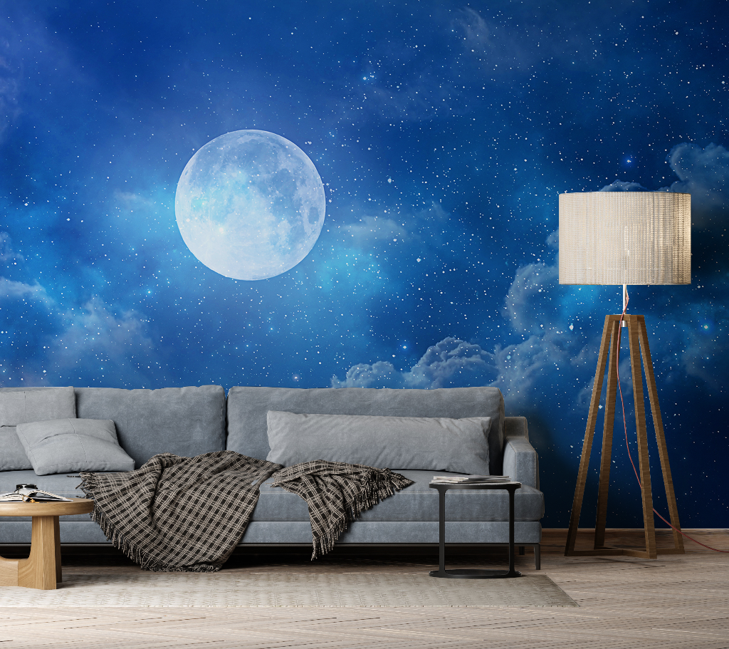 A cozy living room with a gray sofa covered in a checkered throw, wooden floor lamp, and a Decor2Go Wallpaper Mural of Under the Moonlight with a starry night sky and a large full moon.