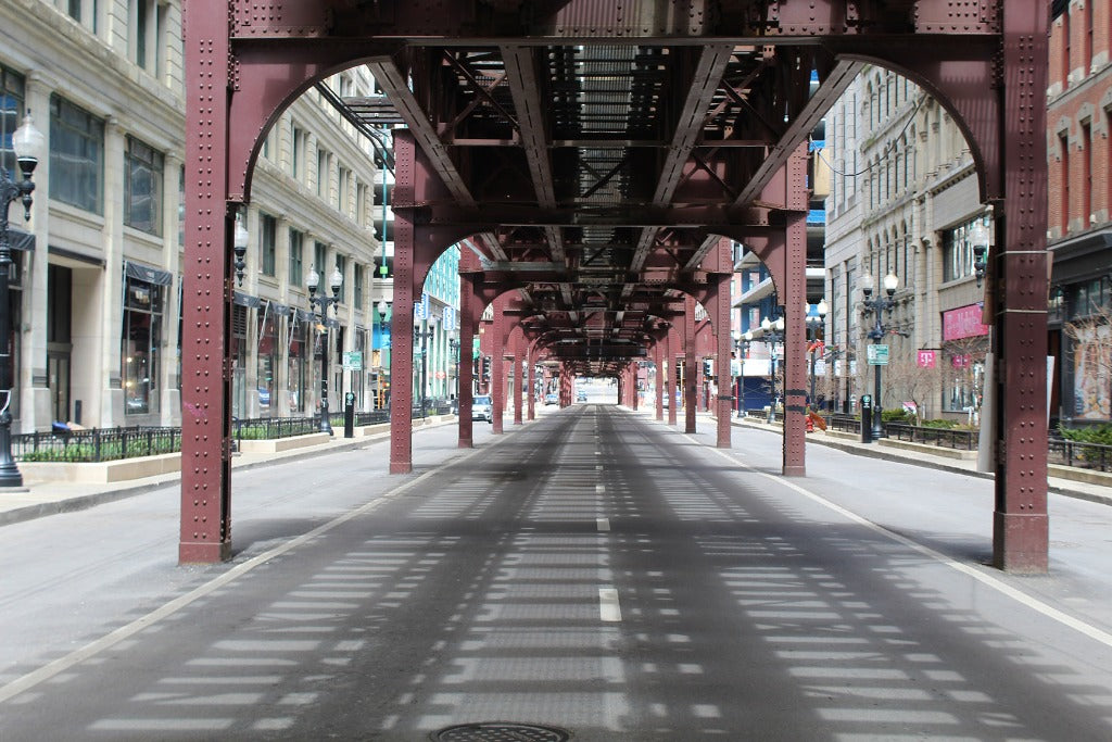 A city street running underneath a Decor2Go Wallpaper Mural with red metal beams creating geometric shadows on the road, flanked by buildings on either side under a clear blue sky.