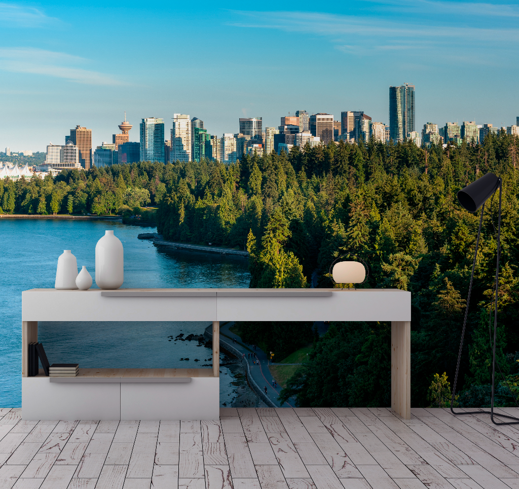 A modern white desk with shelves, holding books and vases, stands on a wooden floor facing a Decor2Go Wallpaper Mural Vancouver Summer Skyline Wallpaper Mural across a bay, surrounded by lush greenery.