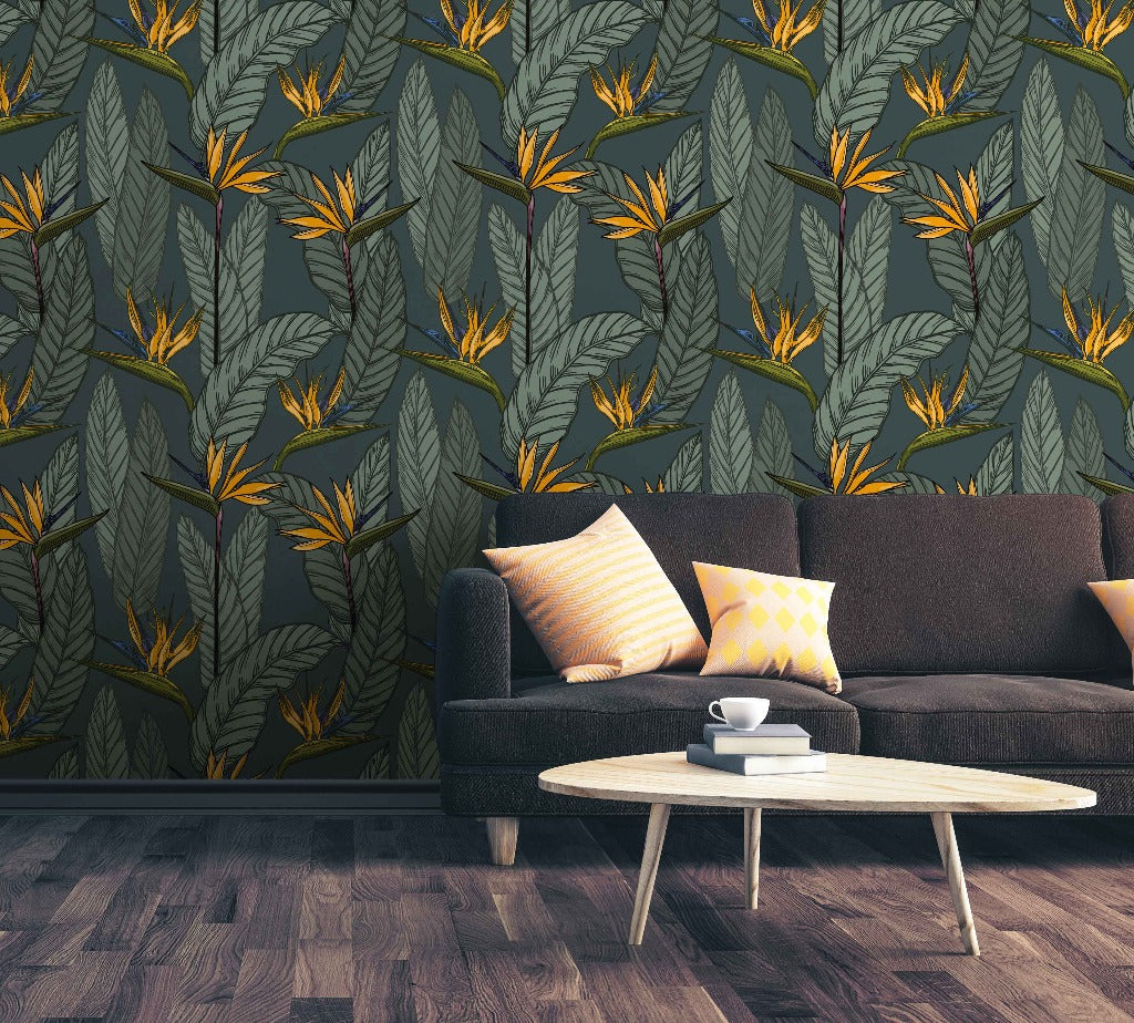 Living Room - A modern living room features a dark brown sofa with yellow and beige patterned cushions. The backdrop showcases a green and yellow strelitzia (bird of paradise) **Vintage Botanical Garden Wallpaper Mural** by **Decor2Go Wallpaper Mural**, a nod to vintage botanical garden designs. A light wood coffee table with a white cup and saucer sits on a dark hardwood floor.