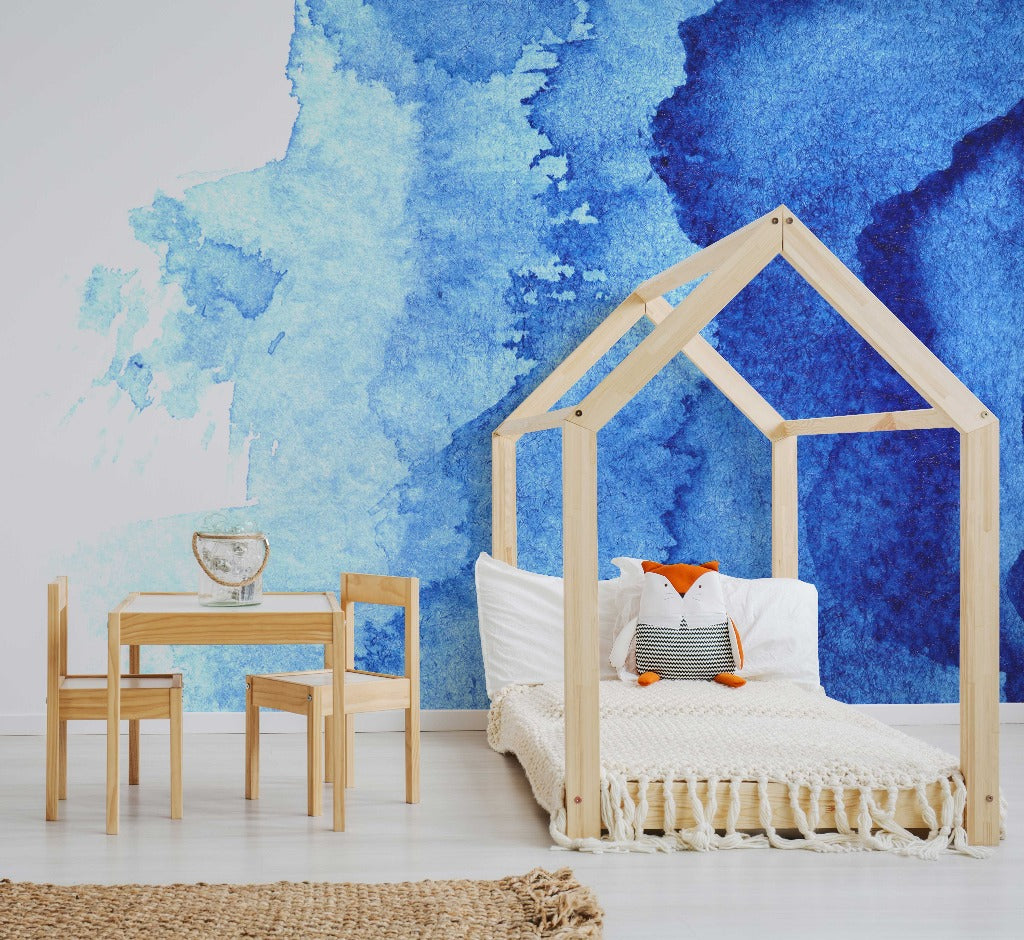 Bedroom - A stylish children's bedroom featuring a wooden house-shaped bed frame with a white mattress, orange pillow, and a fish-shaped pillow. There's a small wooden table and chairs on a rug, next to Decor2Go Wallpaper Mural's Waterblue Ink Wallpaper Mural.