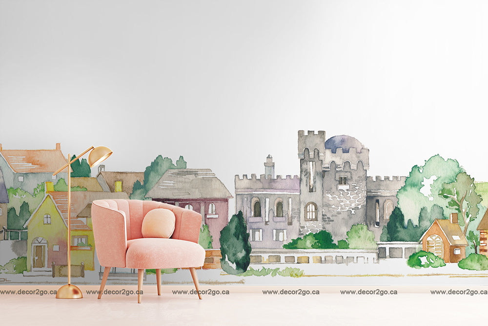 A Watercolor Castle Wallpaper Mural blending indoor and outdoor scenes, suitable as nursery wall decor, featuring a stylish pink armchair and floor lamp inside a room, juxtaposed against a quaint village street with buildings.