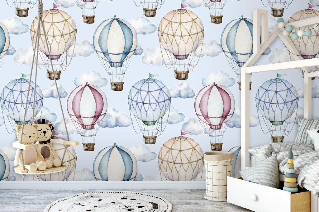 A children's bedroom showcasing a whimsical Decor2Go Watercolor Hot-Air Balloons Wallpaper Mural with varied colorful designs. The room has a wooden crib, storage bins, and plush toys, creating a playful, inviting space.
