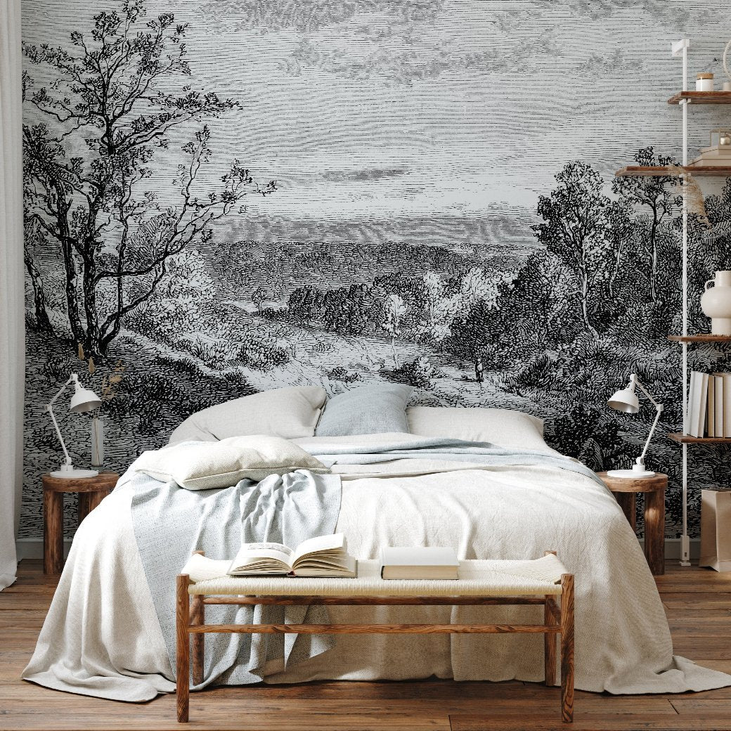 A cozy bedroom with a bed featuring white and light blue linens. The room has wooden side tables, lamps, a bench at the foot of the bed, and shelves with books on the right. The wall behind the bed boasts an ethereal Mystic Lake Wallpaper Mural by Decor2Go Winnipeg in a stunning black-and-white design.