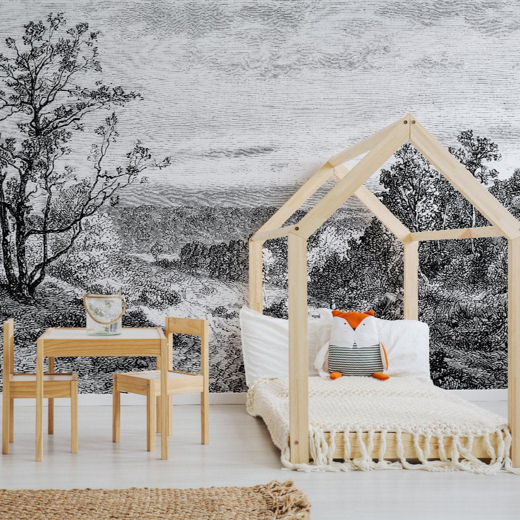 A minimalist children's room features a wooden canopy bed adorned with a fox-shaped pillow. Beside it is a small wooden table and chair set. The background wall is adorned with the Mystic Lake Wallpaper Mural by Decor2Go Winnipeg, which showcases an ethereal black-and-white forest pathway. The floor is white, complemented by a woven rug.