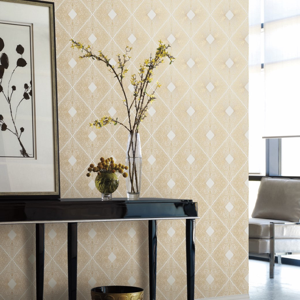 Living Room - corner, a black console table with a glass vase featuring a flowering branch stands beside a decorative ball dish. A framed abstract art piece hangs above, enhanced by York Wallcoverings' White & Gold Harlowe Wallpaper, while a cozy beige armchair invites relaxation