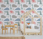 A child's bedroom featuring a wooden house-shaped bed frame with a white cover and fox pillow, a small wooden table and chairs, and walls adorned with Decor2Go Wallpaper Mural depicting vibrant colors and cute animal figures.