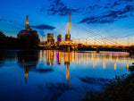 Decor2Go Wallpaper Mural featuring a Winnipeg Twilight scene with a modern suspension bridge, glowing lights, calm water reflection, city skyline, and clear blue sky in the background.